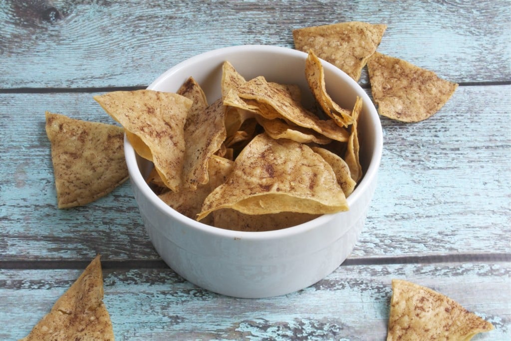 A bowl of baked cinnamon tortilla chips on a blue table. 