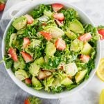 A bowl of brussels sprout kale salad with avocado, quinoa and strawberries.