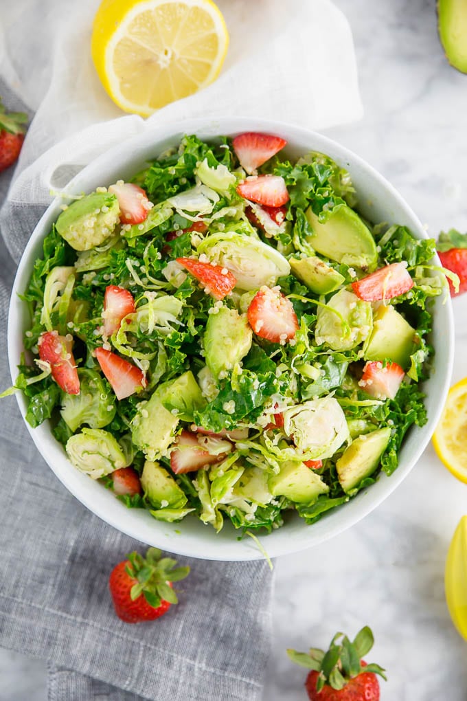 A bowl of brussels sprout kale salad with avocado, quinoa and strawberries.