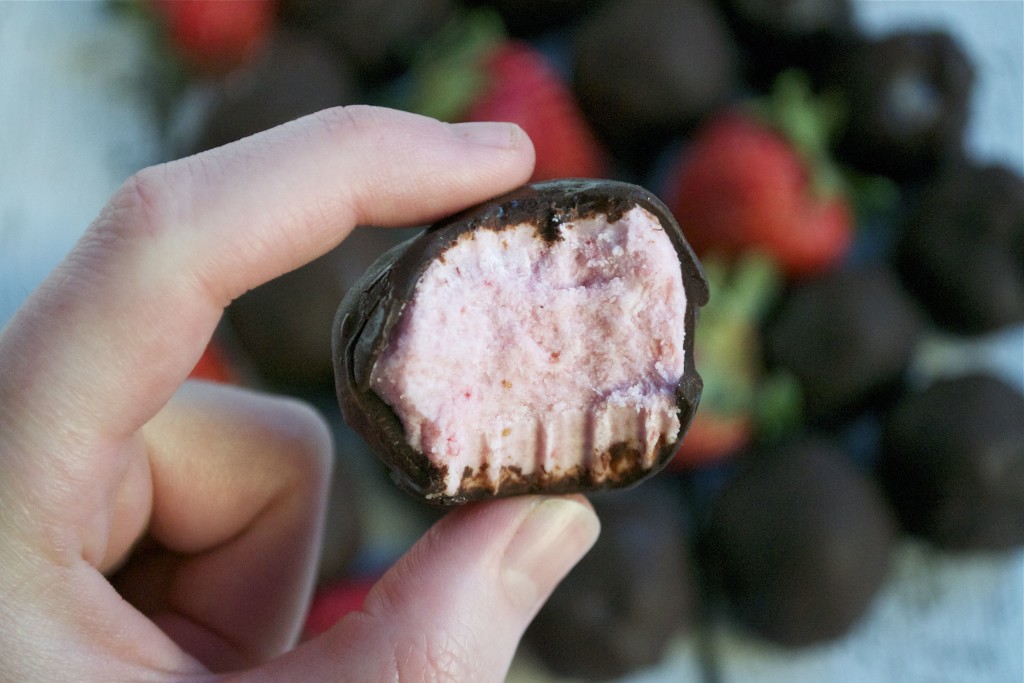 A hand holding a strawberry truffle covered with chocolate.