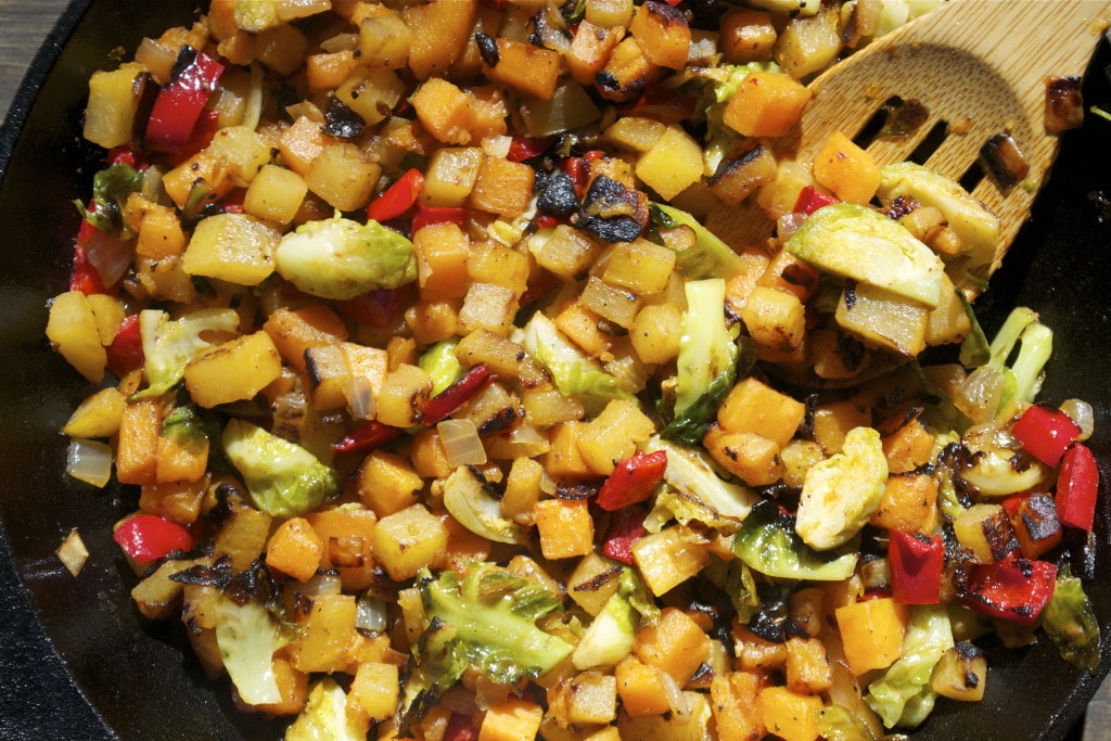 A skillet with rutabaga sweet potato hash with red bell peppers, onion and brussels sprouts.