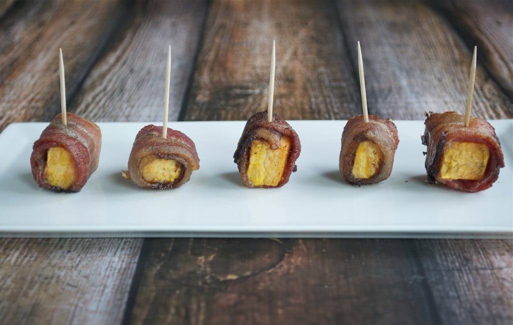 A platter with five bacon wrapped sweet potato bites with toothpicks coming out of them.