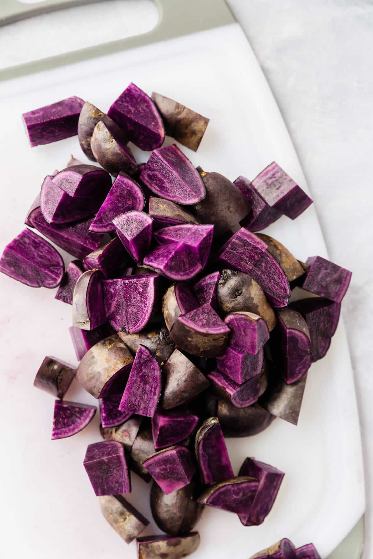 Baby purple potatoes diced on a white cutting board.