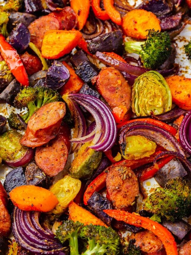 Roasted onions, carrots, broccoli, sausage, brussels sprouts, and red bell peppers on a sheet pan.