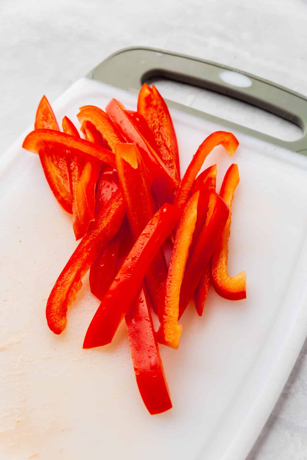 Red bell pepper julienned on a white cutting board.