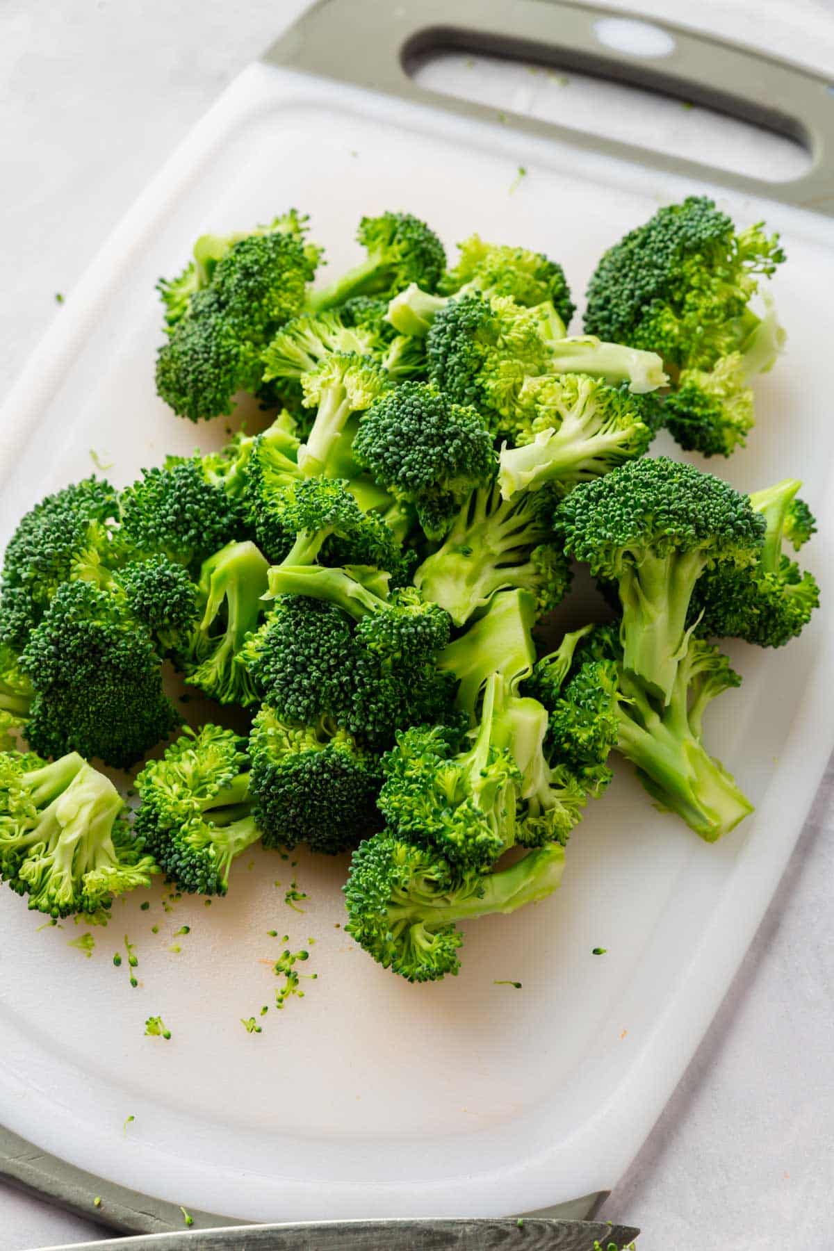 Broccoli cut into small florets on a white cutting board.