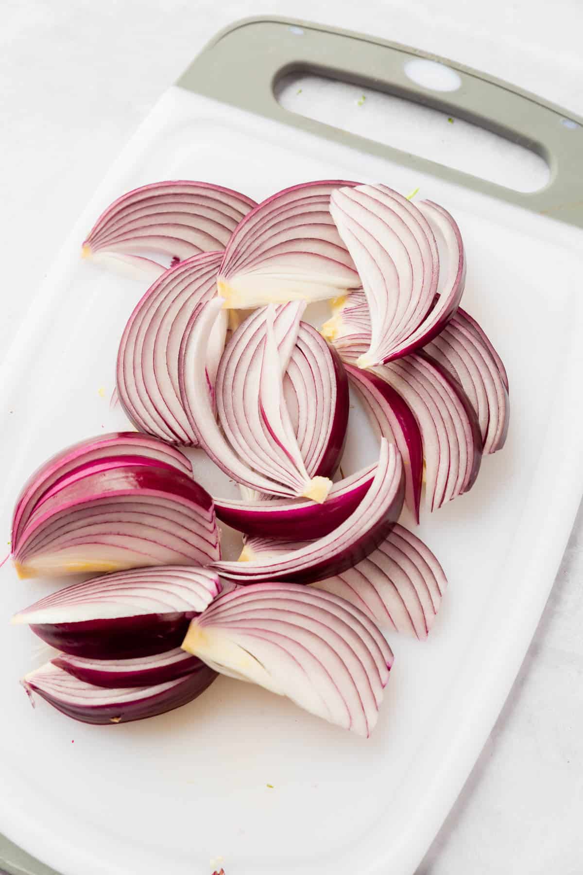 Red onion sliced on a white cutting board.
