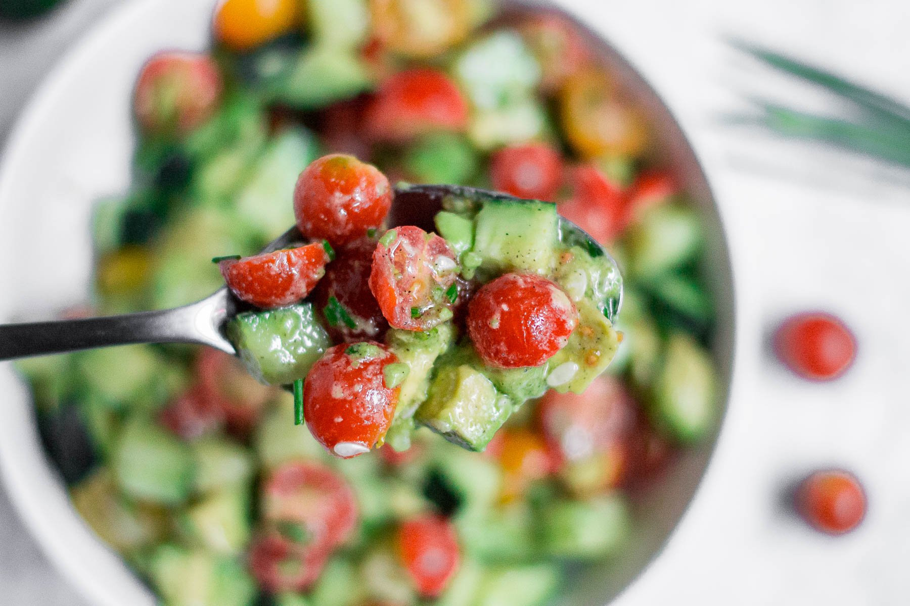 A spoon filled with tomato avocado cucumber salad. 