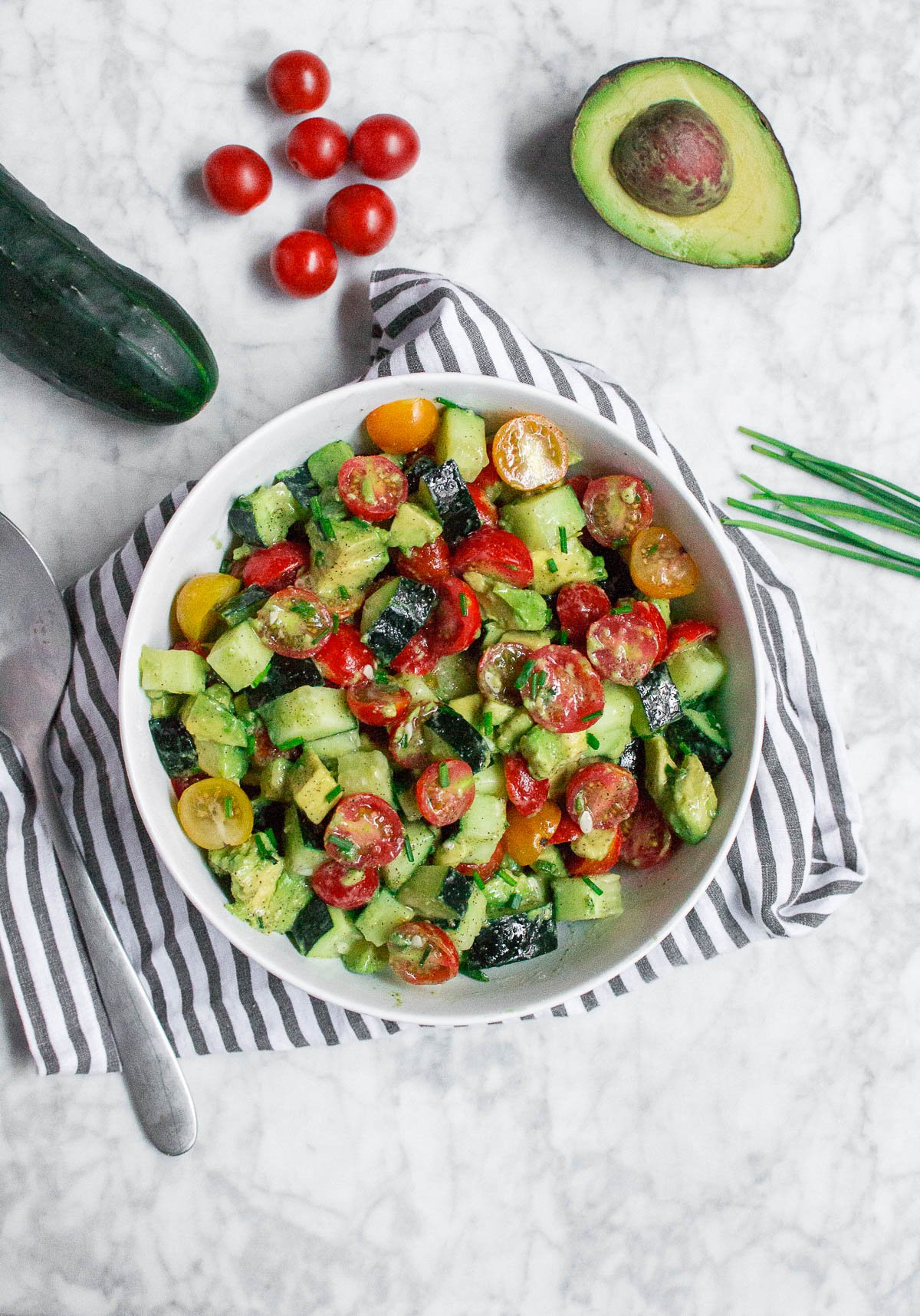 An aerial view of a bowl of cucumber avocado tomato with chives and lemon dressing. 