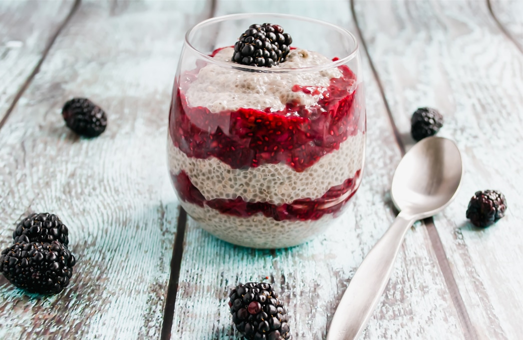 A clear glass filled with 5 layers of chia seed pudding and blackberry chia jam and topped with a fresh blackberry.