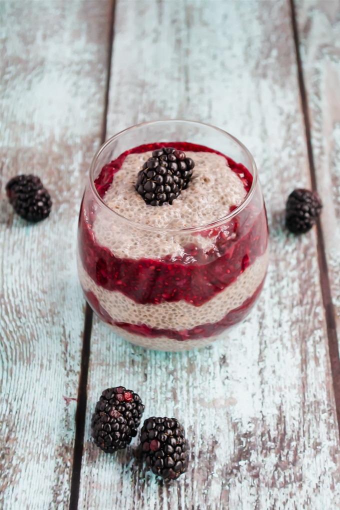 A glass of layers of chia seed pudding and blackberry chia jam and topped with a fresh blackberry.