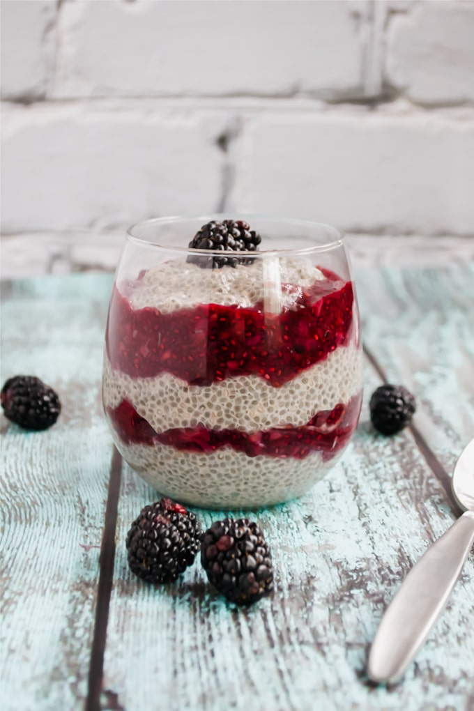 A wine glass with layers of chia pudding and blackberry chia jam topped with a fresh blackberry. 