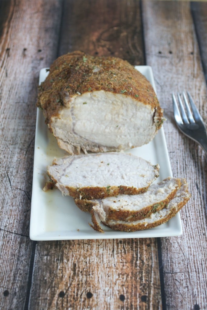 A white rectangle platter with spice rubbed pork loin with a few slices cut off of it. 