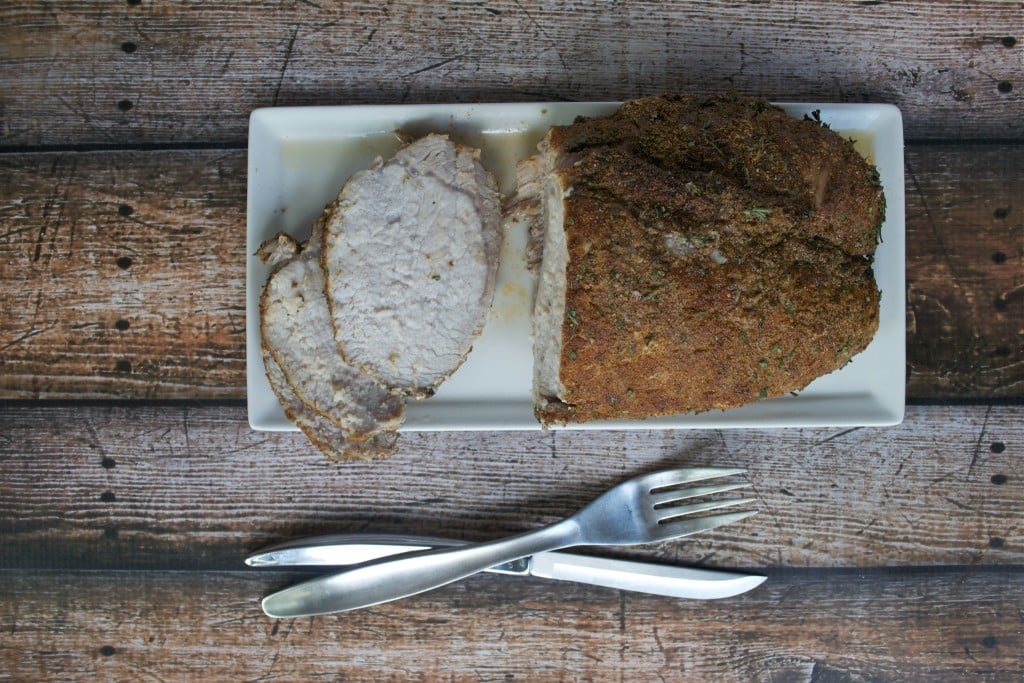 An overhead view of a spice rubbed pork loin with a few slices cut off on a rectangle white platter.