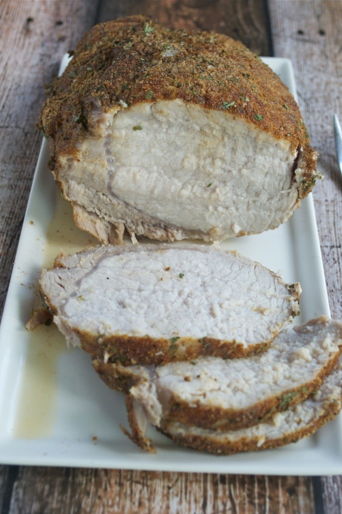 Spice rubbed pork loin with a few slices cut off on a white rectangle platter.