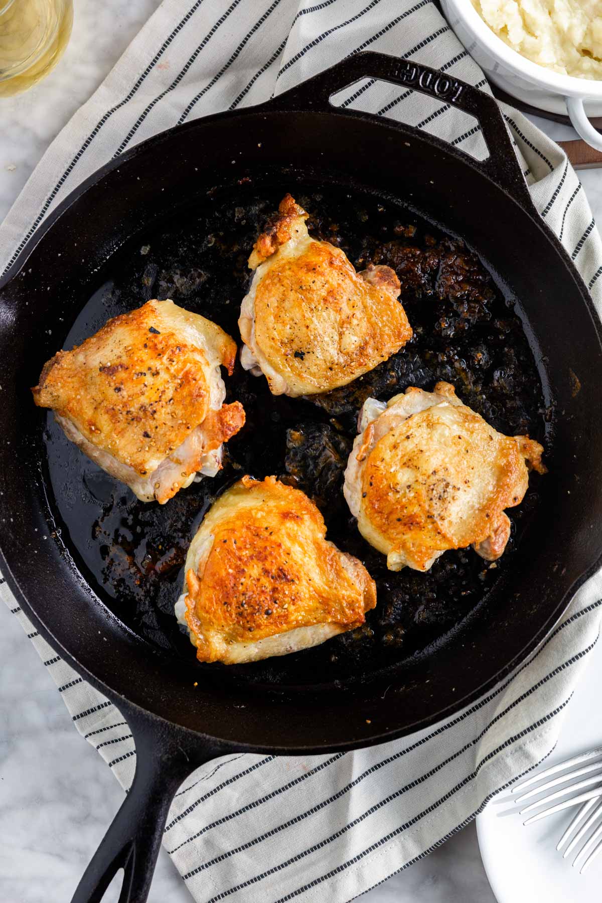 A cast iron skillet with four crispy chicken thighs with golden brown skin after baking in the oven. 