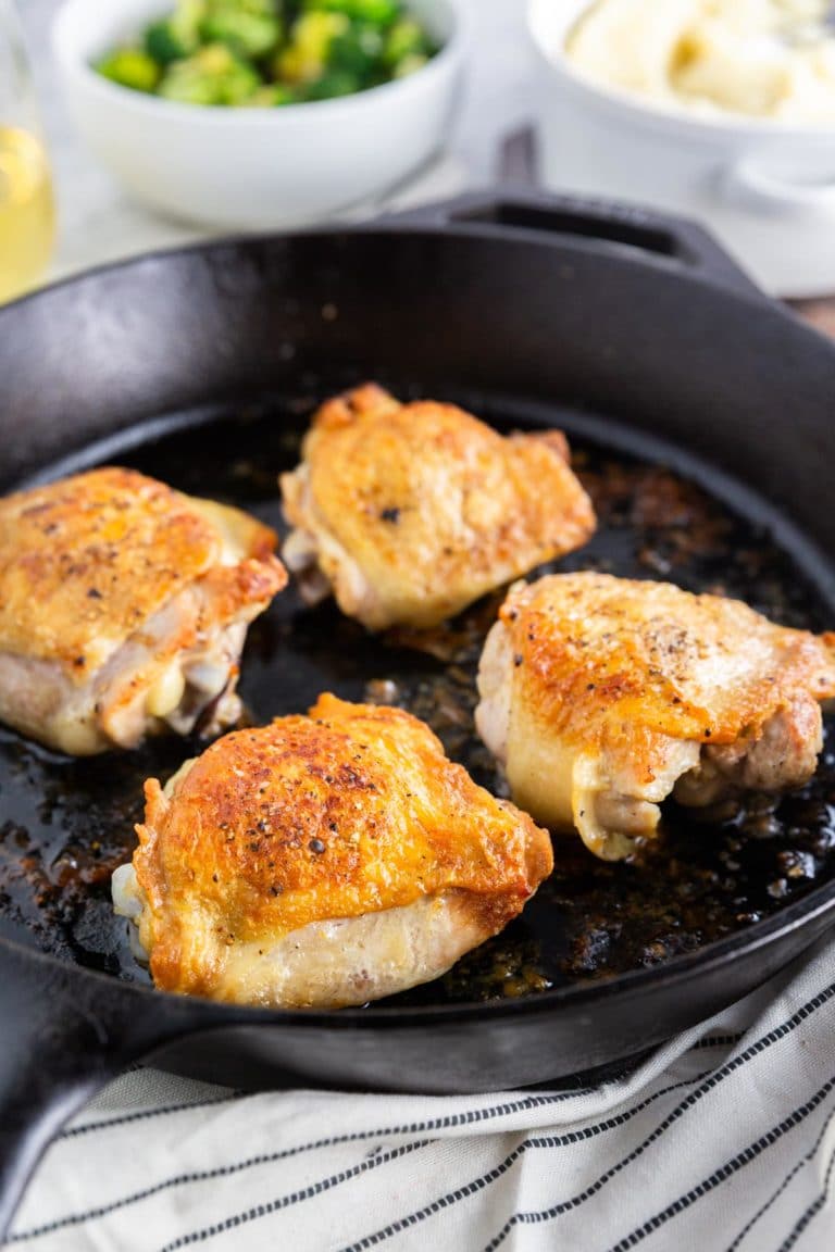 A photo of a large cast iron skillet with roasted chicken thighs in it topped with salt and pepper.