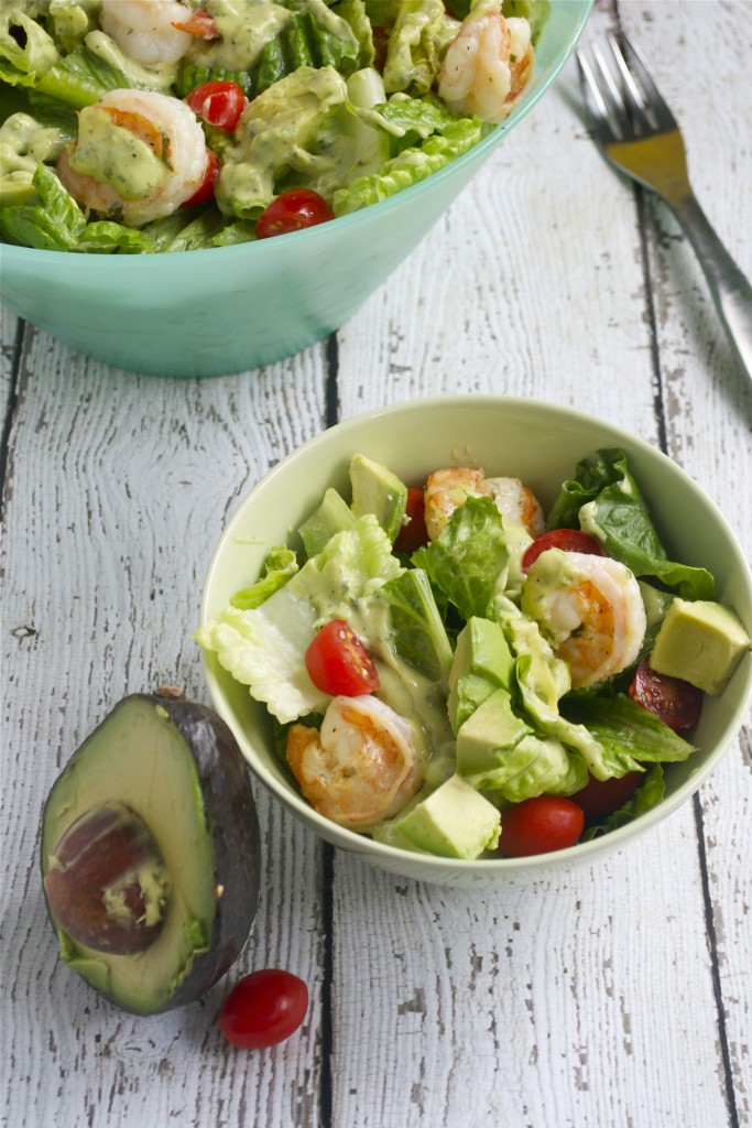 A bowl of salad with shrimp, cherry tomatoes, avocado and creamy dressing.