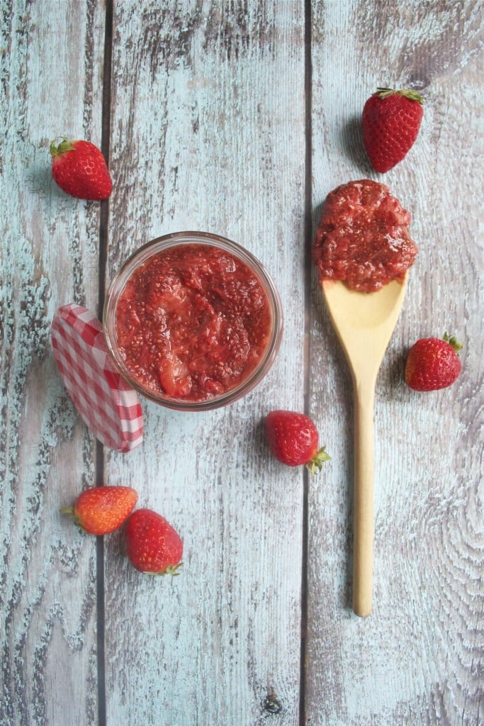 An overhead view of a jar of strawberry chia jam and a wooden spoon of jam on it.