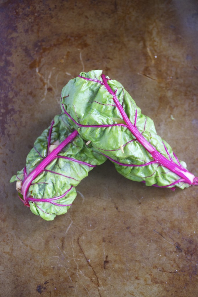 Two rainbow chard wraps leaning on top of each other on a baking sheet. 