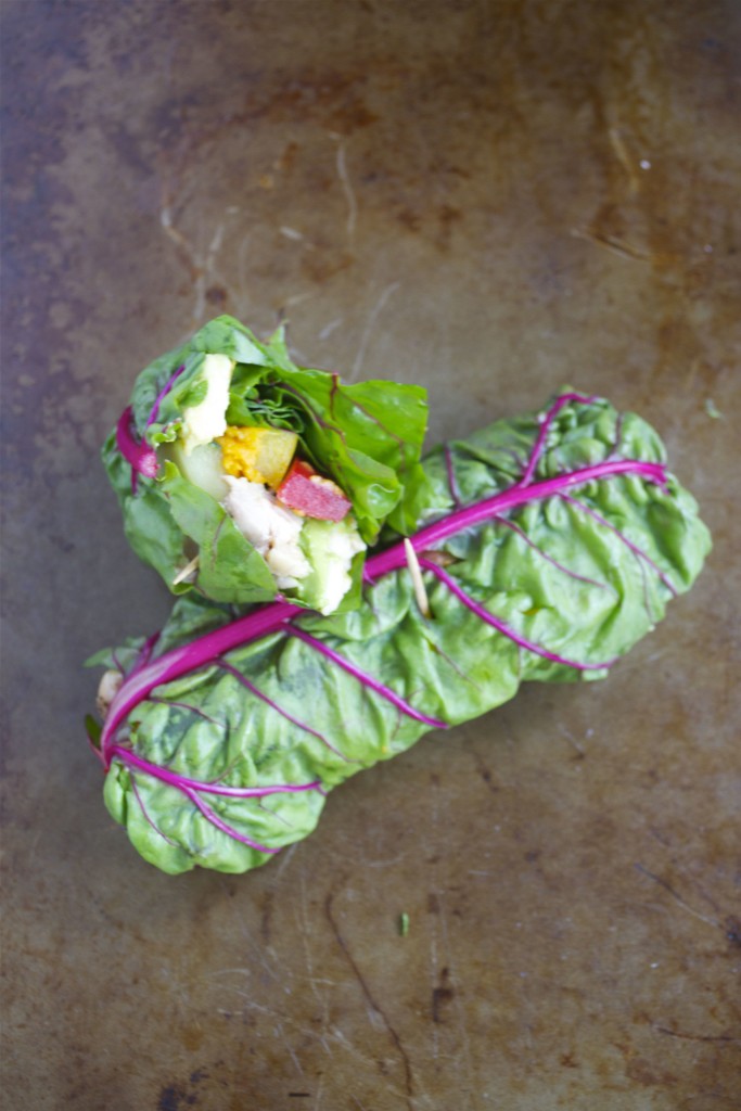 Two rainbow chard vegetable wraps leaning on top of each other with the top one cut in half to see the inside.