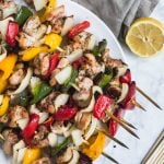 Aerial view of chicken kabobs on wooden skewers with colorful red, yellow and green peppers and onions with half of a lemon.