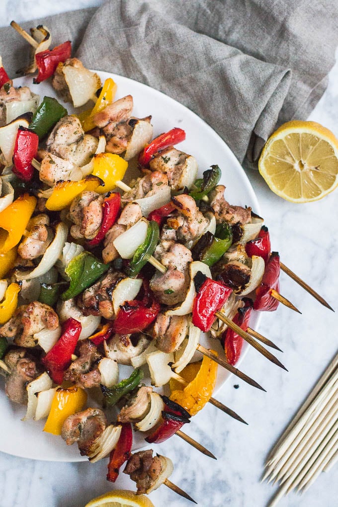 Aerial view of chicken kabobs on wooden skewers with colorful red, yellow and green peppers and onions with half of a lemon. 