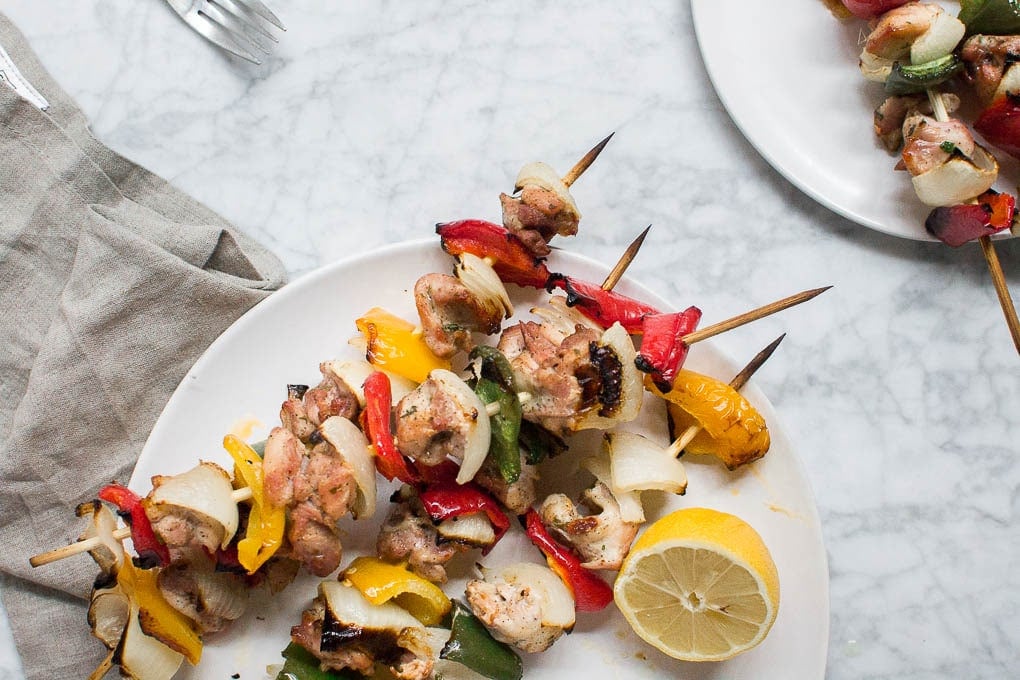 Aerial view of chicken kabob skewers on a platter with a lemon wedge and a small plate of kabobs for serving. 