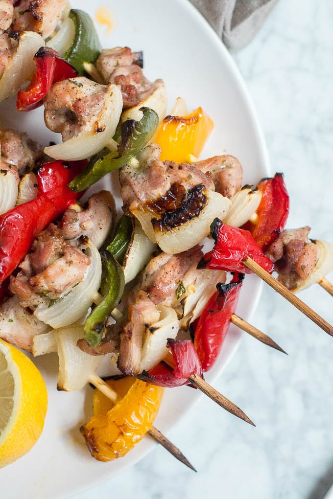 Plate of chicken kabobs with peppers and onions with a lemon wedge.