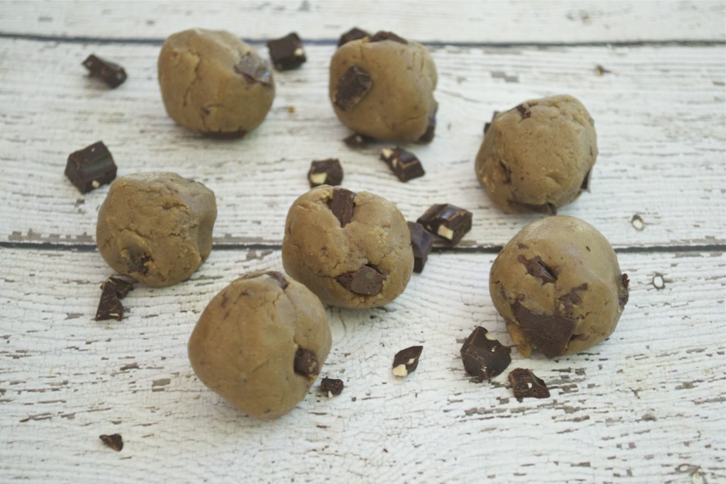 Raw edible cookie dough balls on a wood table with chocolate chunks.