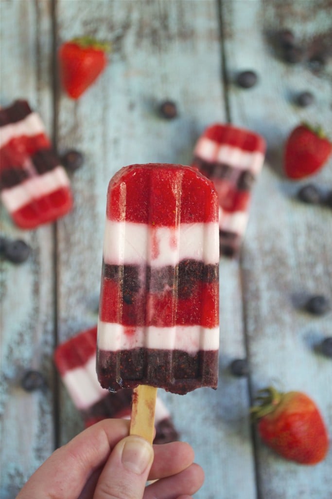 A hand holding a layered red, white and blue popsicle. 