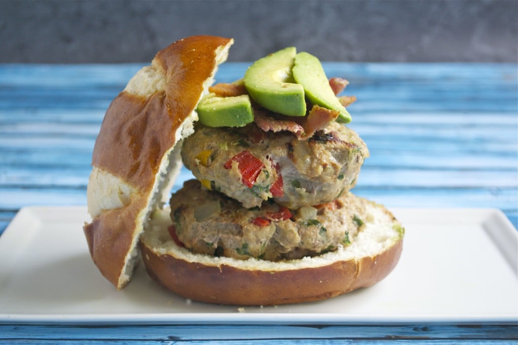 A stack of two turkey veggie burgers on a bun and topped with bacon and avocado. 