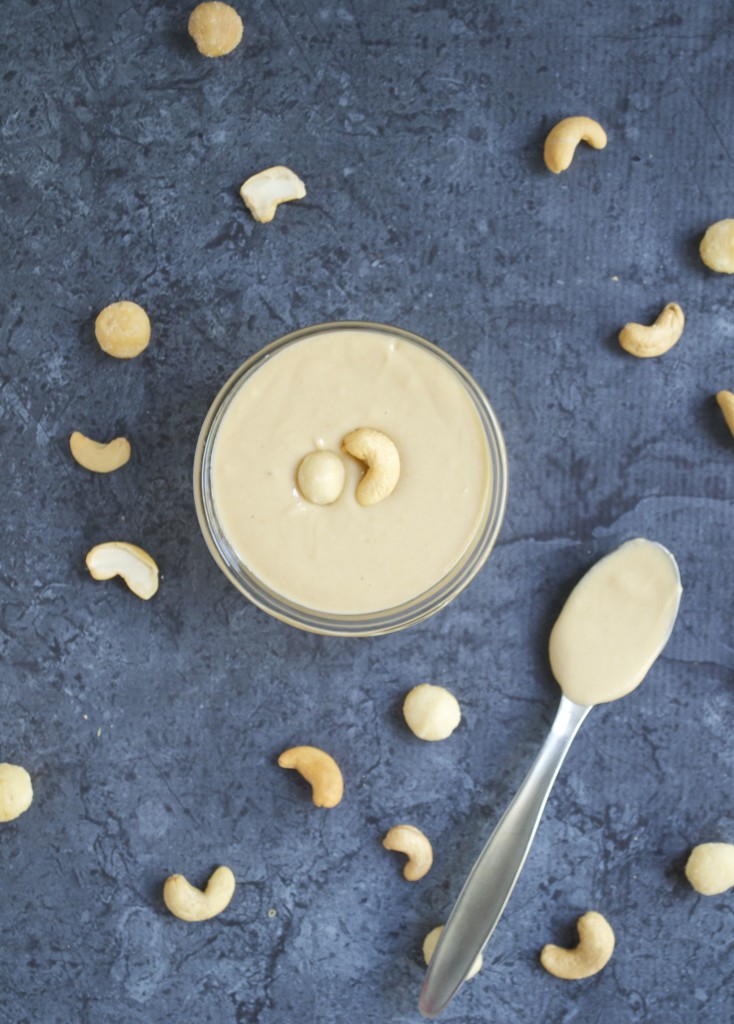 A glass bowl of macadamia nut cashew butter with a spoon on the table.