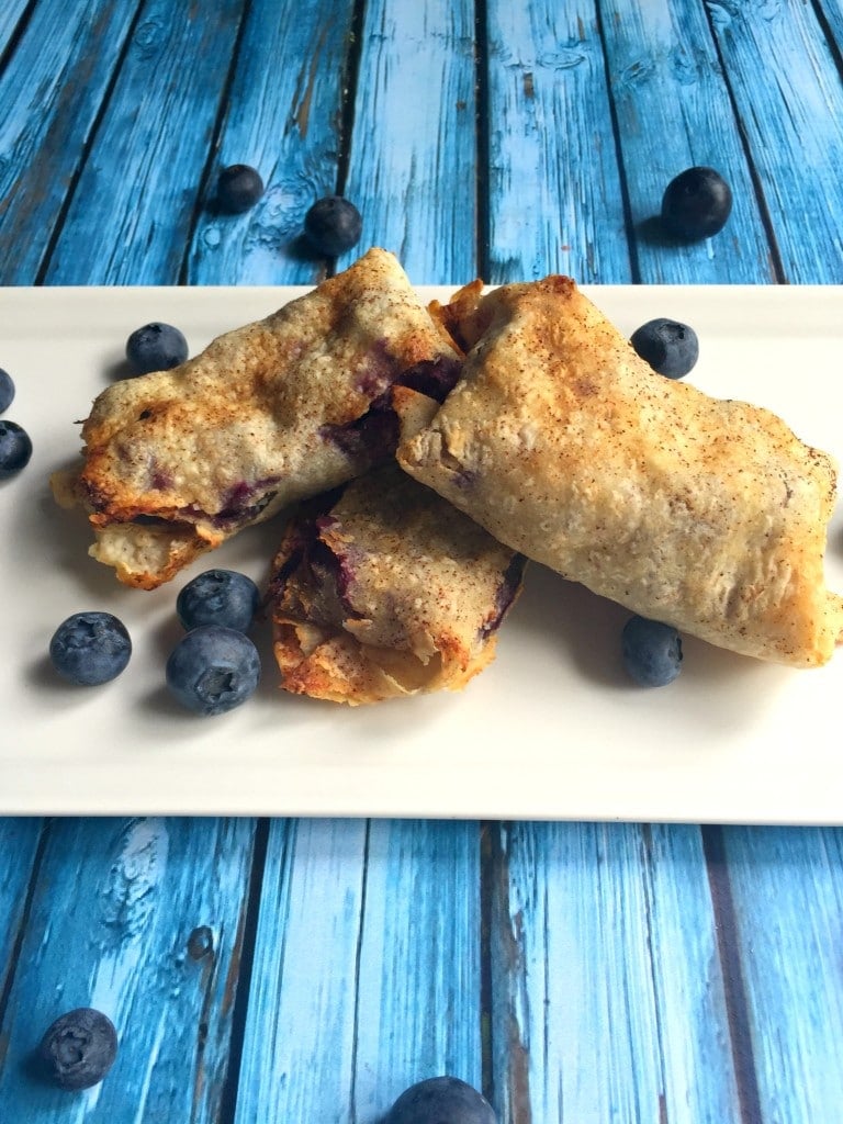 A pile of three blueberry tortilla pockets on a white platter with fresh blueberries.