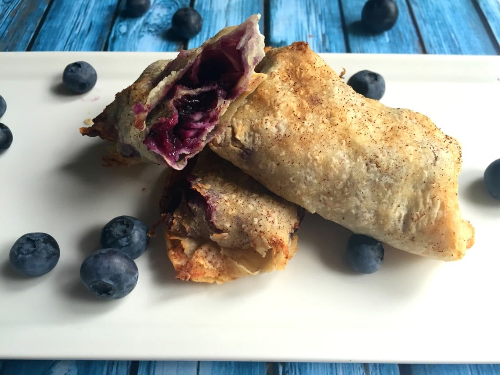 A stack of three blueberry tortilla pockets on a white plate with fresh blueberries.