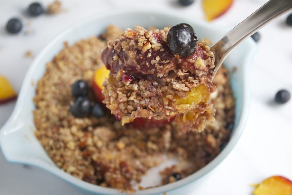 A spoonful of blueberry peach crisp being held over a casserole dish.