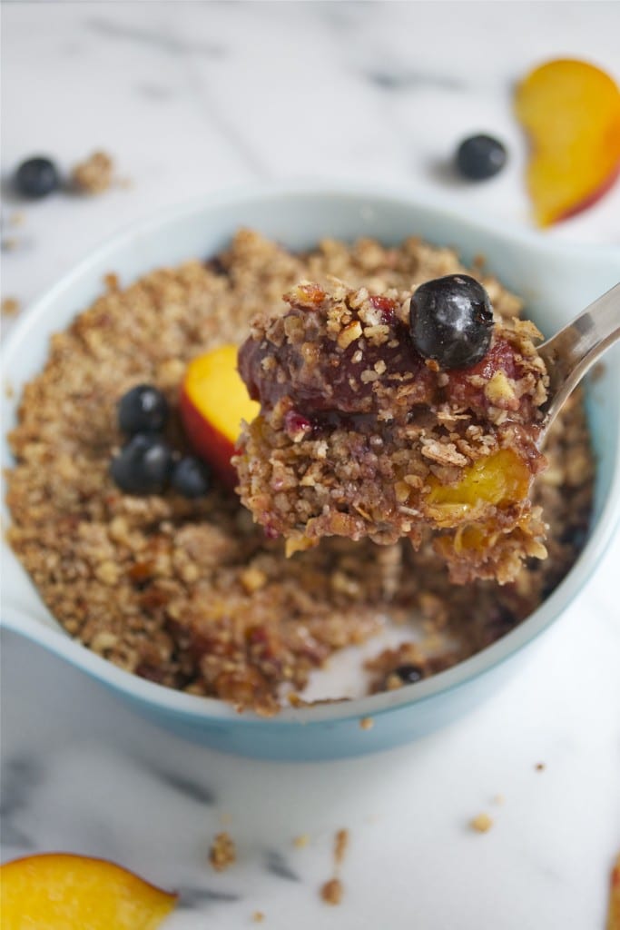 A spoon of blueberry peach crisp over a small casserole dish of crisp.