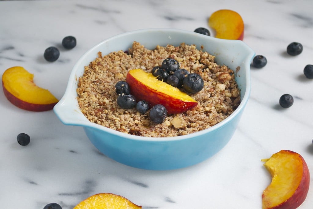 A small casserole dish of blueberry peach crisp with fresh peaches and blueberries on top. 