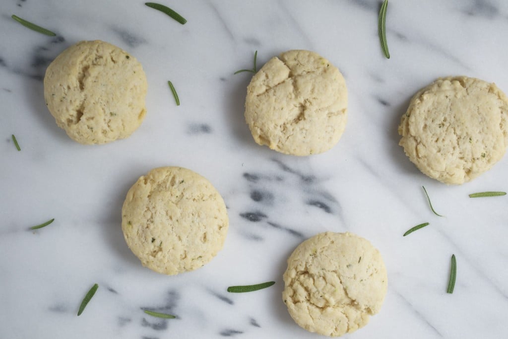 An overhead view of rosemary biscuits on a marble table with fresh rosemary sprigs.