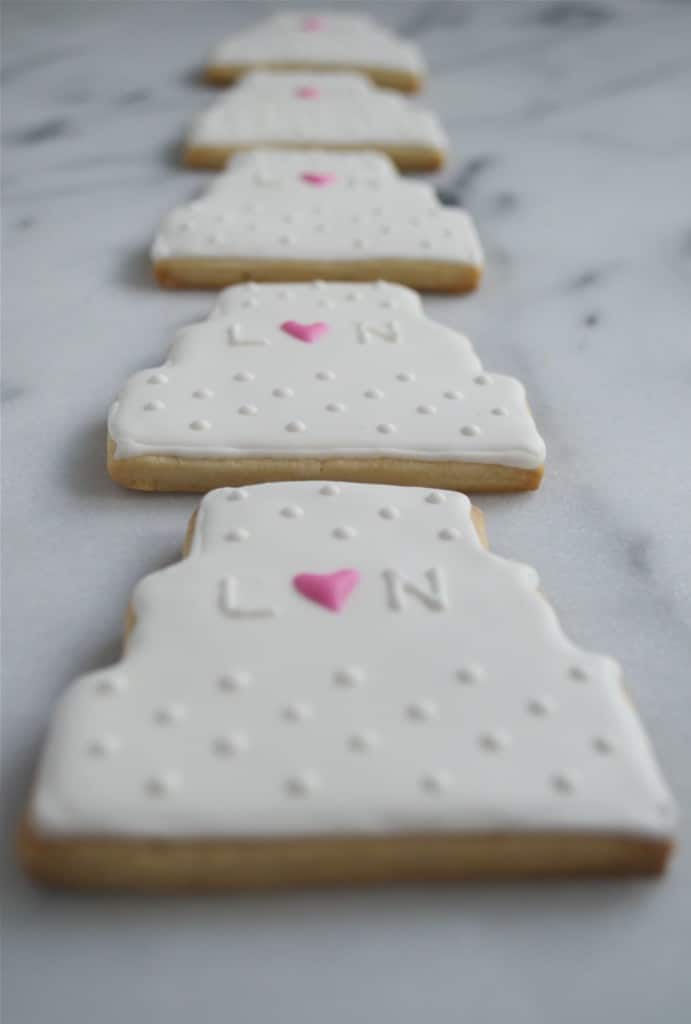 A row of wedding cake sugar cookies decorated with royal icing on a marble table.