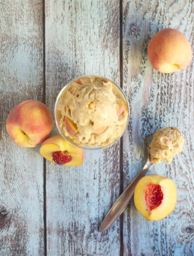 An overhead view of a bowl of vegan peach ice cream with fresh peach haves and a spoon on the table.
