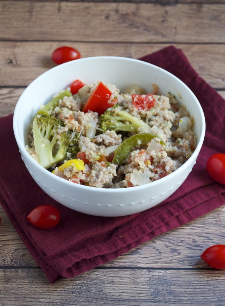 A bowl with quinoa, ground turkey, broccoli, peppers, and cherry tomatoes on a red linen napkin.