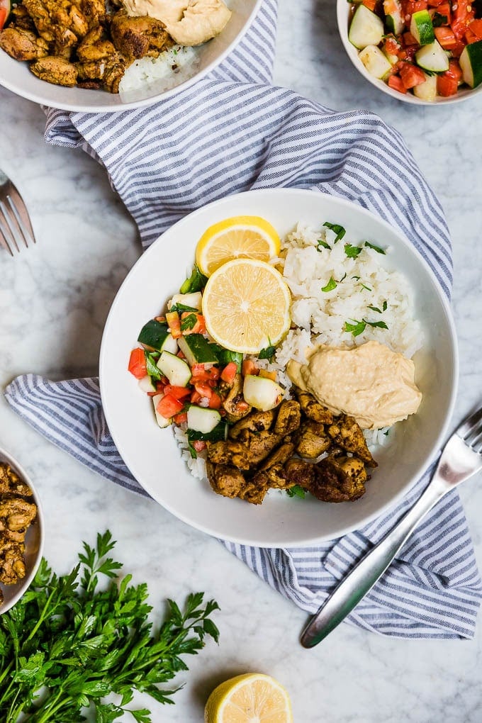 Easy meal prep mediterranean chicken bowls with rice, hummus and tomato cucumber salad. 