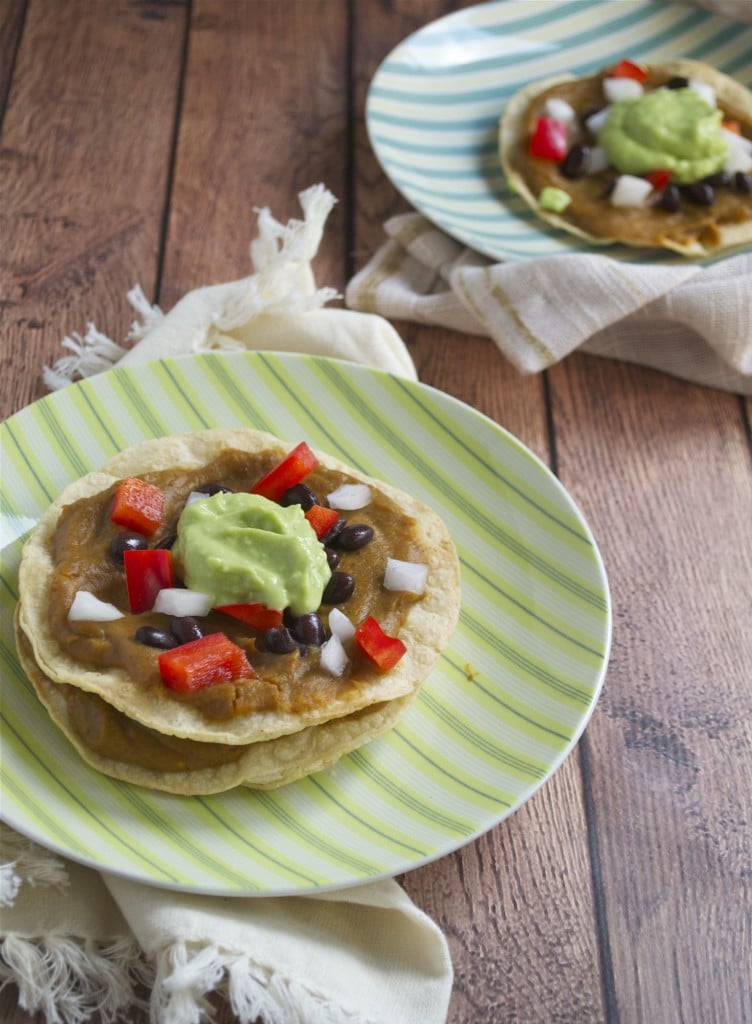 A plate of sweet potato tostadas topped with avocado cream, red onions, black beans and red bell peppers. 