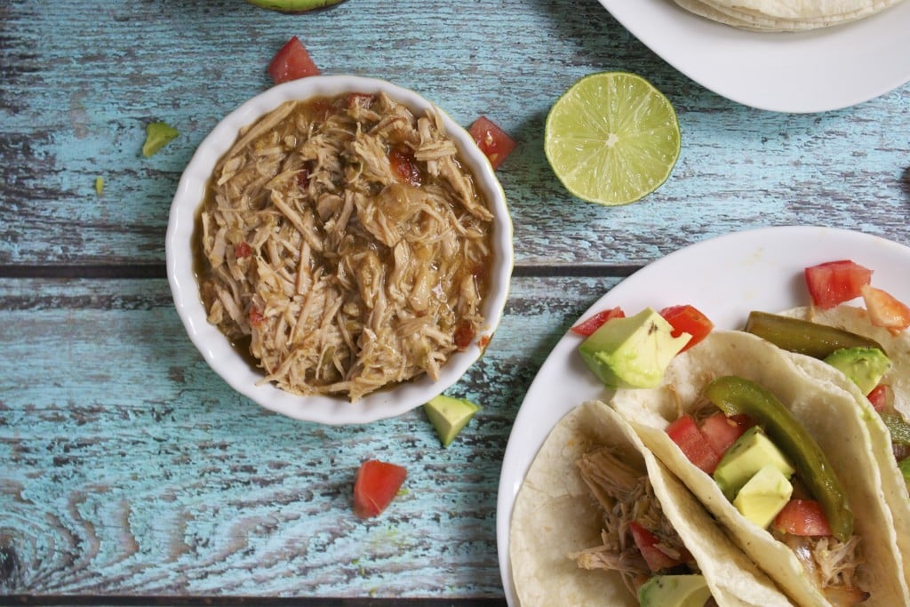 A ramekin of pulled pork with a plate of pulled pork tacos and lime wedges on the side.