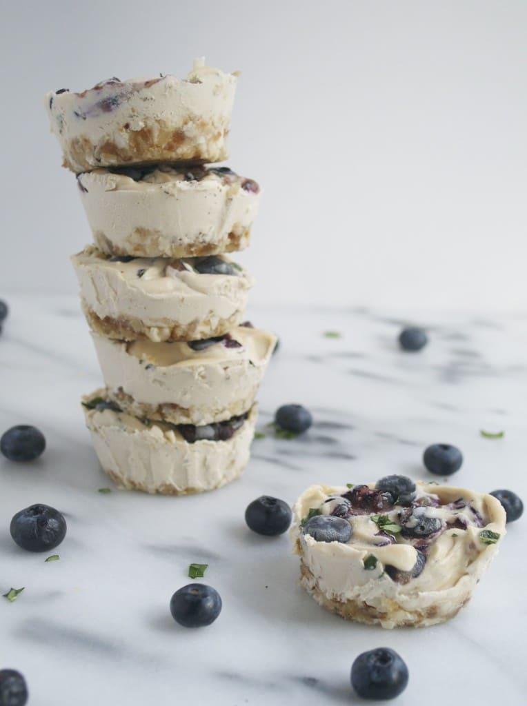 A mini vegan blueberry basil cheesecake in front of a large stack of mini cheesecakes.