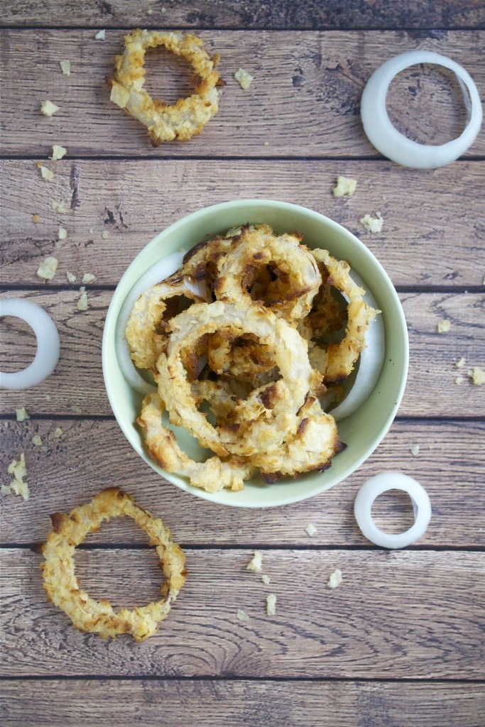 A bowl of baked onion rings on a wood table.