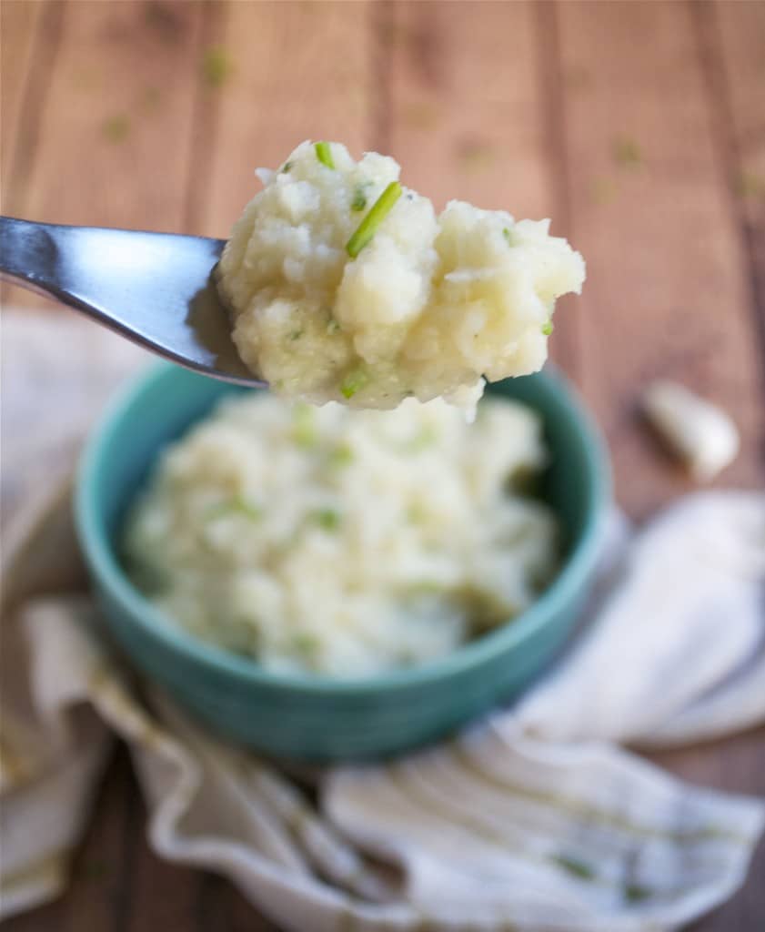 A fork full of cauliflower parsnip mash over a bowl.