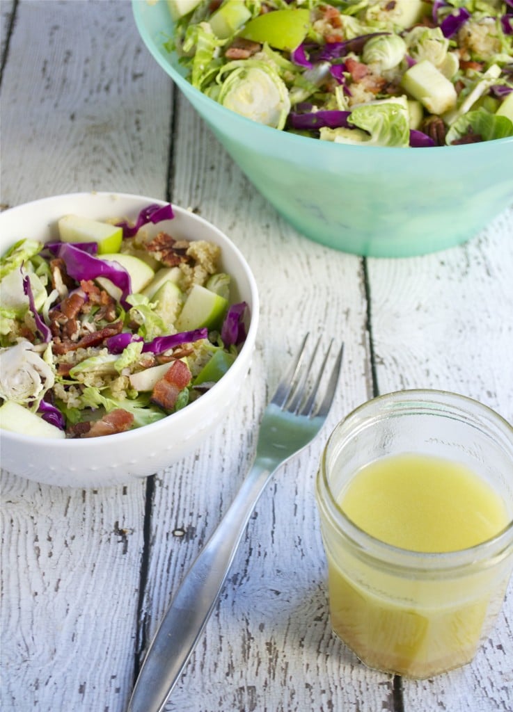 A bowl of shaved brussels sprout salad topped with walnuts and diced apple and a side of apple cider vinaigrette. 