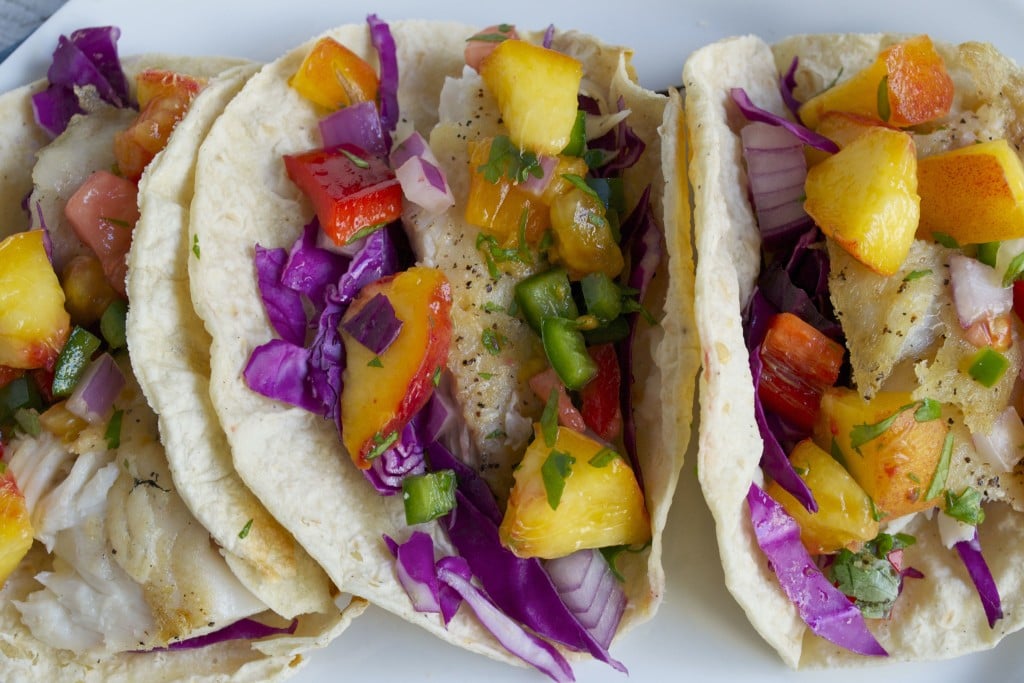 Three tilapia tacos topped with peach salsa and red cabbage.